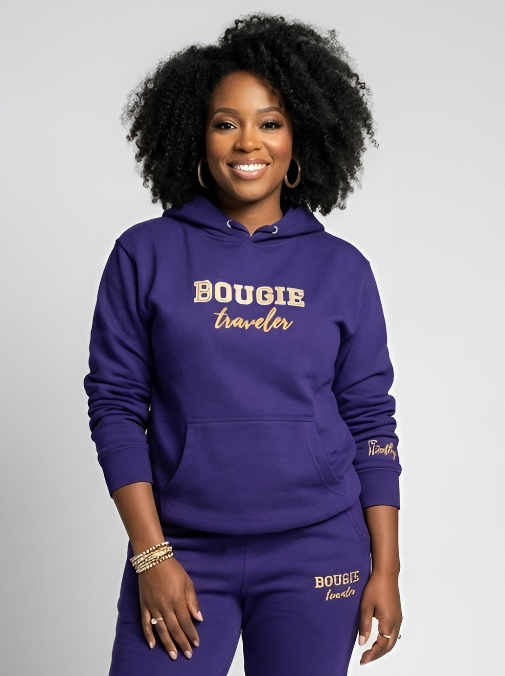 Woman wearing a purple 'Bougie Traveler' hoodie and pants on a white background